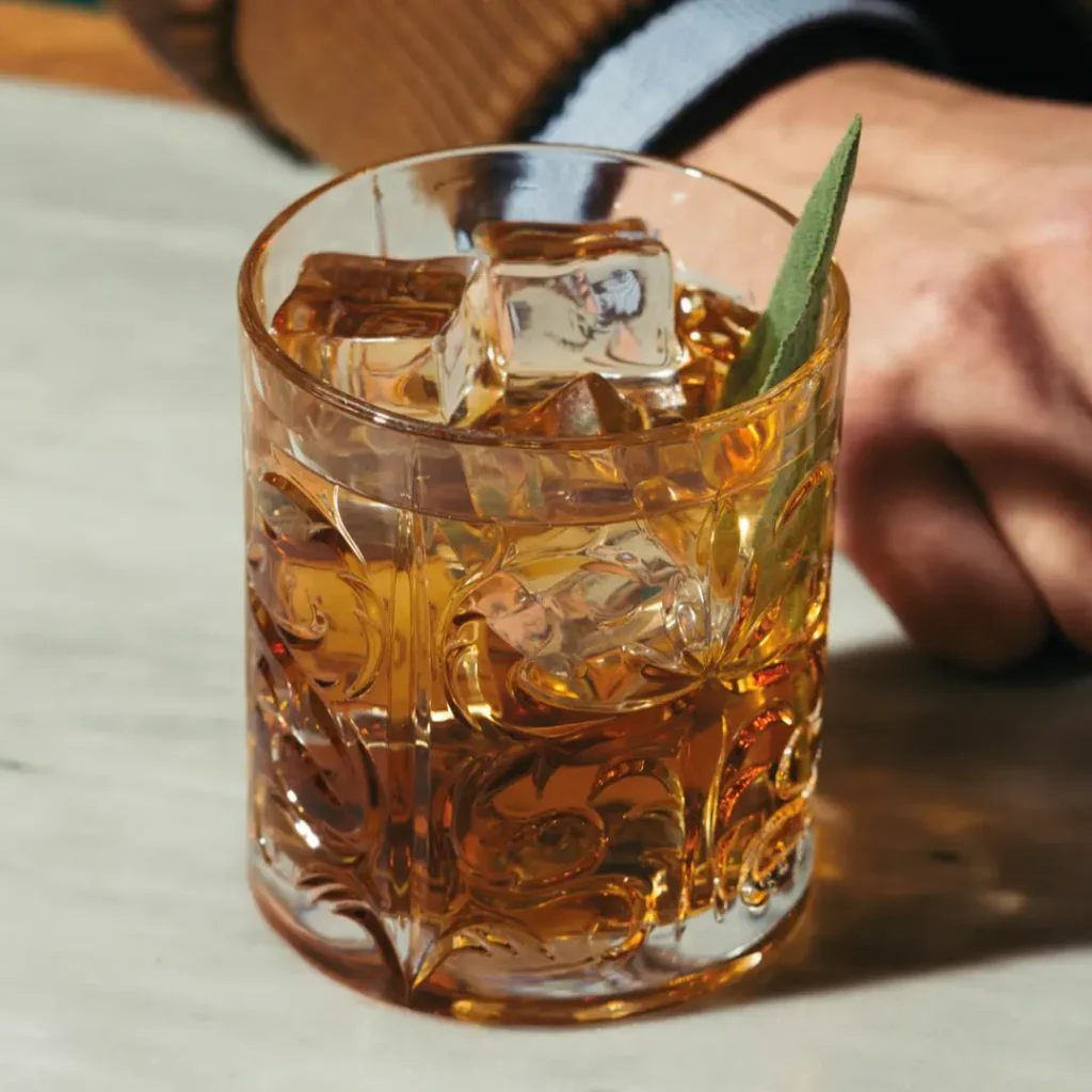 Close-up eines Cocktails mit großen Eiswürfeln und Blattgarnitur in einem verzierten Tumblerglas