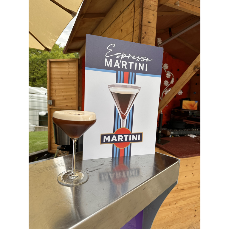 Ein frisch zubereiteter Espresso Martini steht auf einer Edelstahltheke vor einem Cocktail-Promotion-Schild