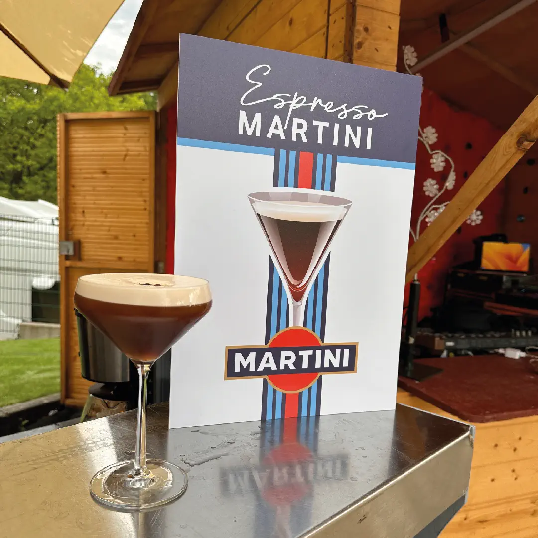 Ein frisch zubereiteter Espresso Martini steht auf einer Edelstahltheke vor einem Cocktail-Promotion-Schild
